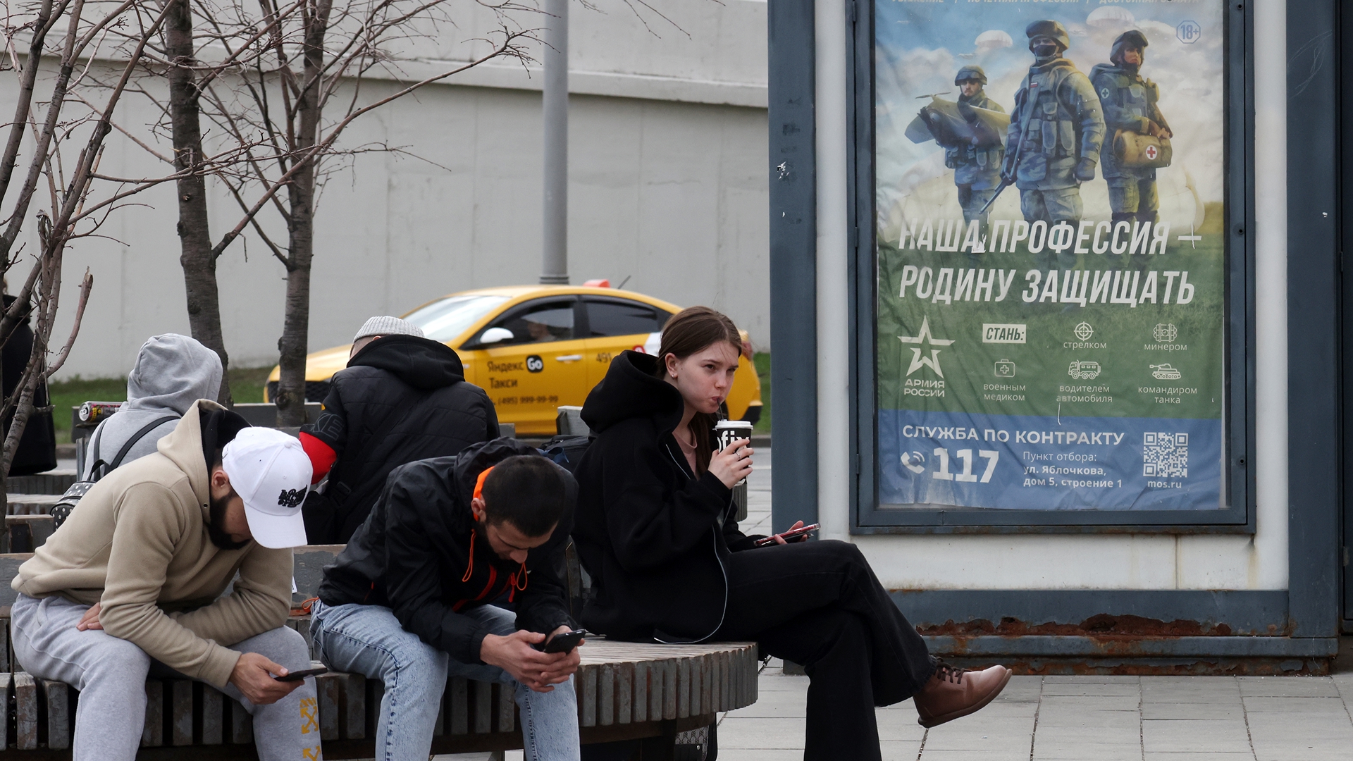 Ludzie siedzą na ławce w pobliżu wojskowego billboardu propagandowego zachęcającego do udziału w rosyjskiej inwazji na Ukrainę; Moskwa, Rosja, 11 kwietnia 2024 r. (fot. Getty Images)