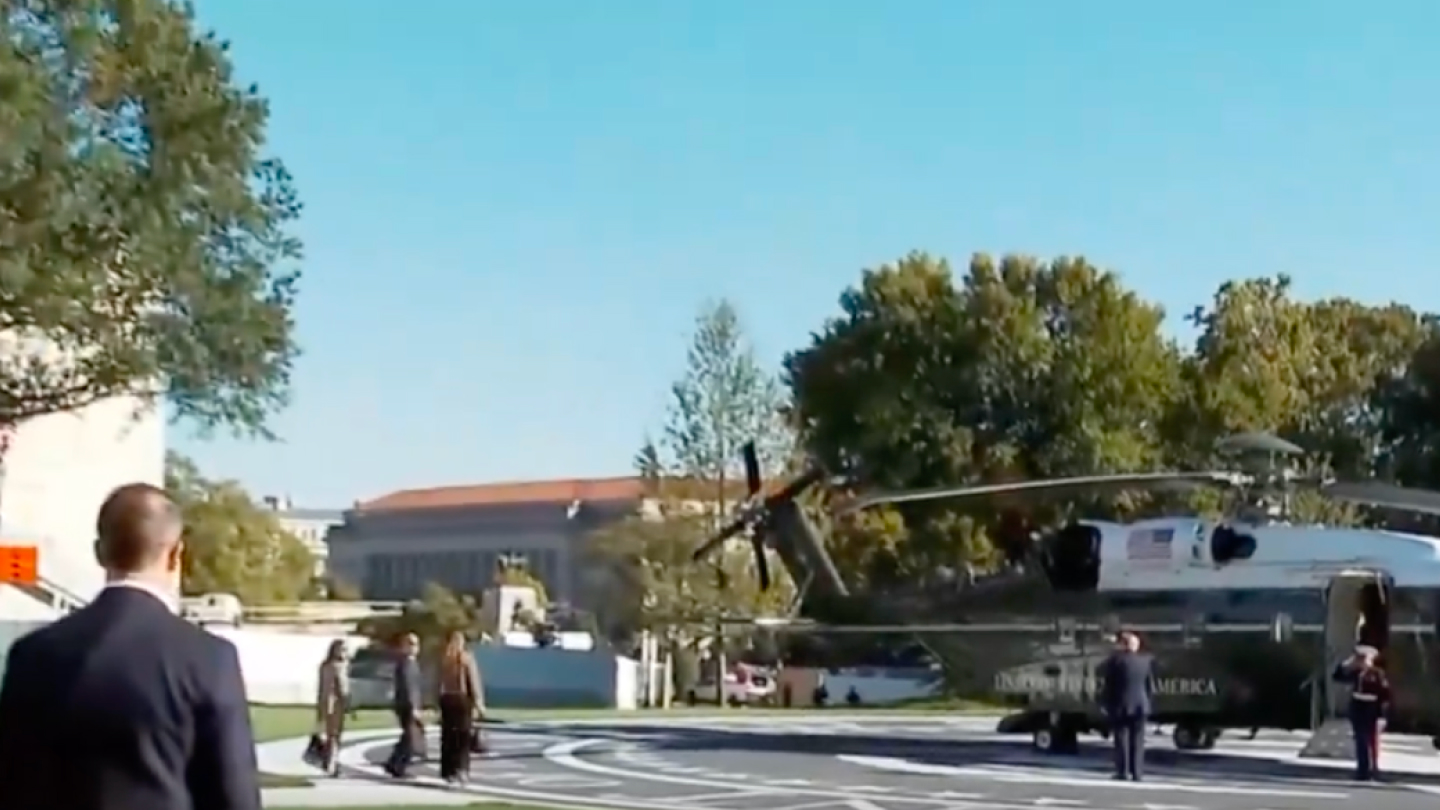 Donald Trump macha przed wejściem na pokład helikoptera Marine One. Szerszy kadr pokazuje osoby znajdujące się w pobliżu lądowiska. Źródło: X.